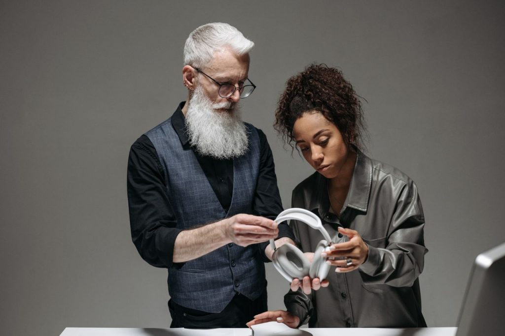 Senior caucasian man and black woman discussing headphones in an office setup.